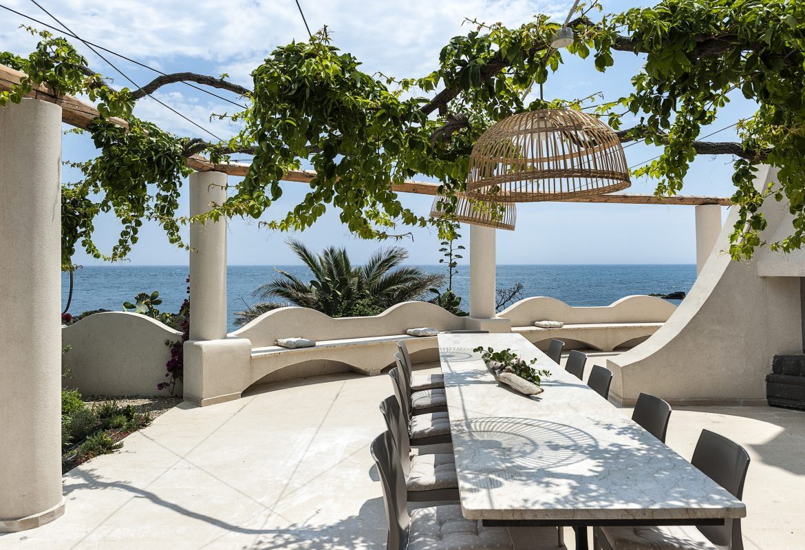 A dining table under a vine-covered pergola on a terrace above the sea at Villa Naxos, near Taormina