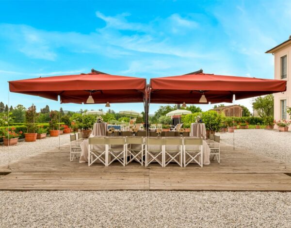 A long table under red umbrellas, laid for dinner in the garden of Daniela near Lucca
