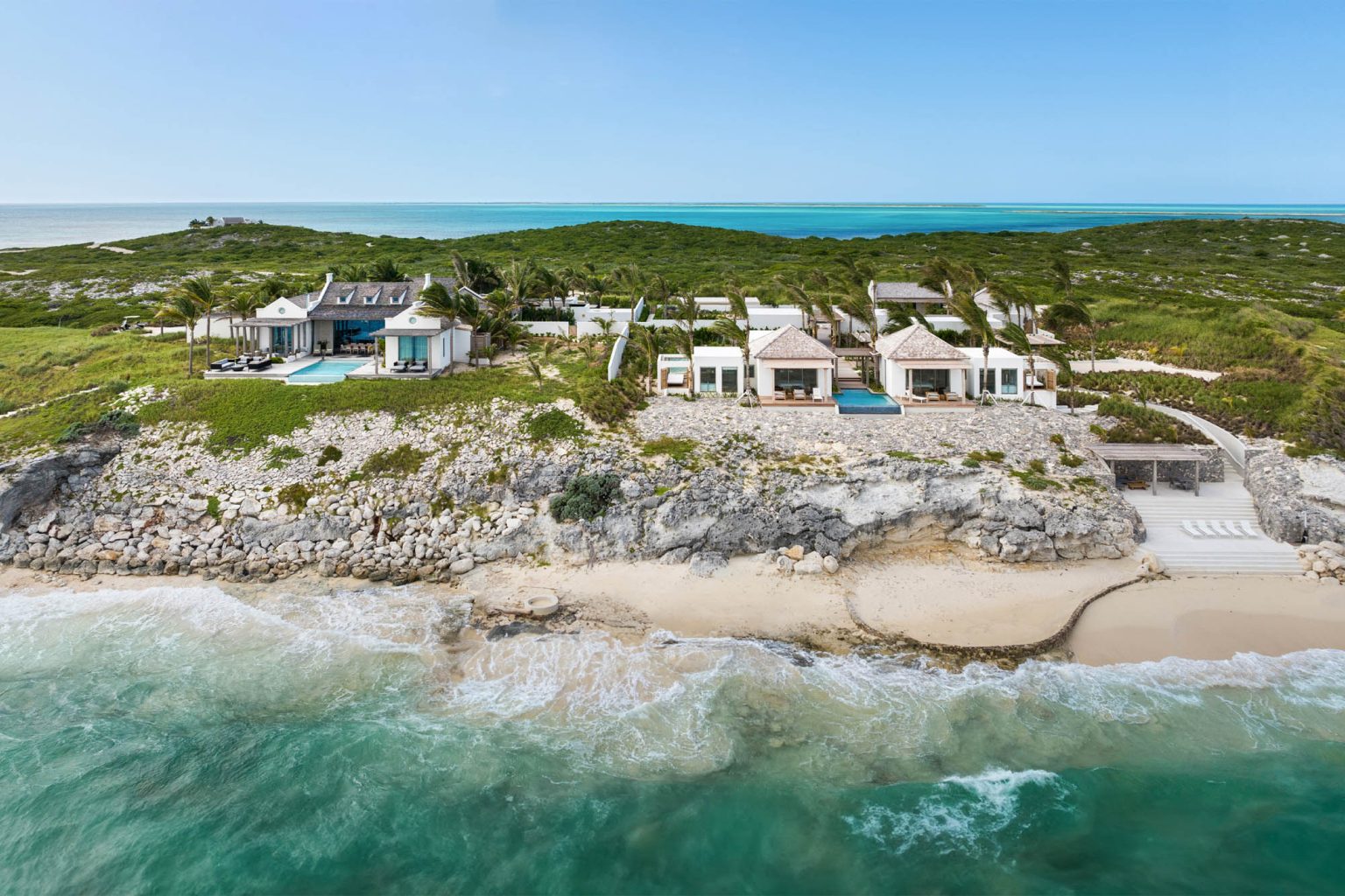 Aerial view of the Dream Estate villas above a rocky shore and a white beach on Ambergris Cay