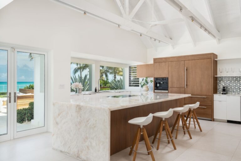 The kitchen at Villa Salacia, with a long marble island, white bar stools and glass doors open to the palms