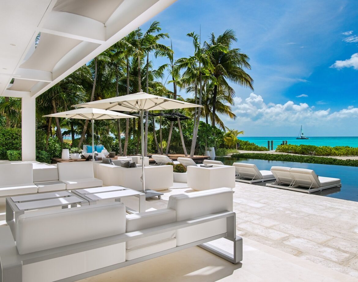 a white lounge chairs and umbrellas by a pool Turks and Caicos villas