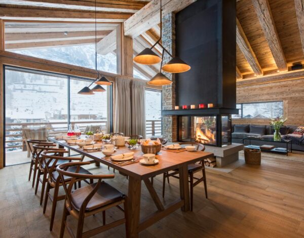 A long dining table beside an open fire in a timber chalet
