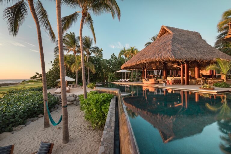 The thatched palapa and pool of Koko Retreat among the palms in Punta Mita