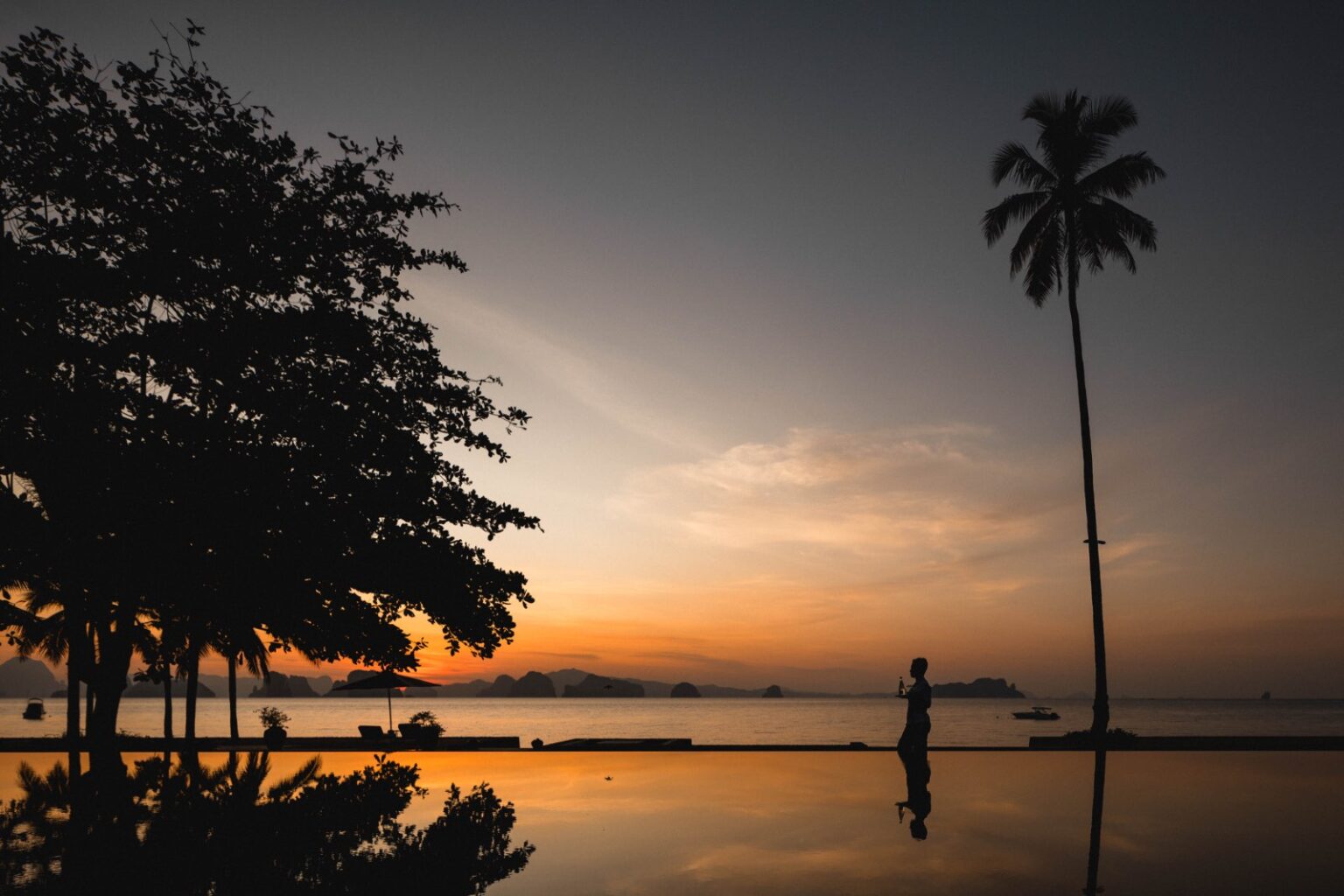 Luxury Villa Rentals and Mansions for Rent | Haute Retreats | 18 A guest at the edge of an infinity pool at sunset, palms silhouetted over the bay