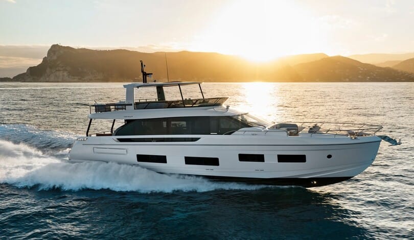 A white Azimut Fly 82 flybridge yacht cruising at sunset, with a headland behind